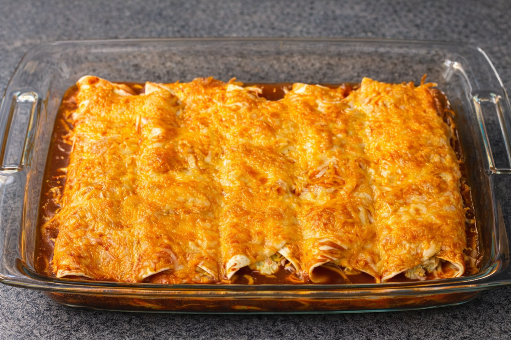 Creamy red chicken enchiladas baked with cheddar and mozzarella in a glass baking dish